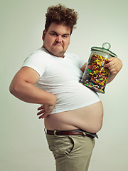 Image showing Candy, jar and portrait of silly man in studio for snacks, sweets and dessert in container. Comic, goofy and overweight, isolated and plus size person with glass for unhealthy diet on background