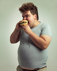 Image showing Obesity, weight gain and hamburger for man in studio with food for unhealthy eating, plus size and greed. Overweight person with meal in mouth and fat stomach for expression humor and comedy indoor