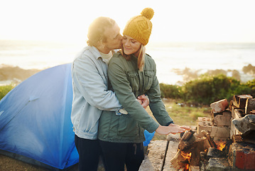 Image showing Happy couple, kiss and bonding together by campfire, outdoor and romantic getaway with camping in forest. Man, woman and love on vacation on weekend break, countryside and travel in woods for sunset