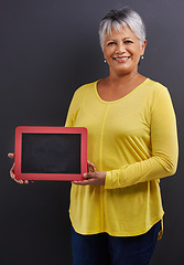 Image showing Smile, chalk board and portrait of woman in studio with mockup space for marketing, promotion or advertising. Happy, mock up and senior female person with frame for news isolated by black background.