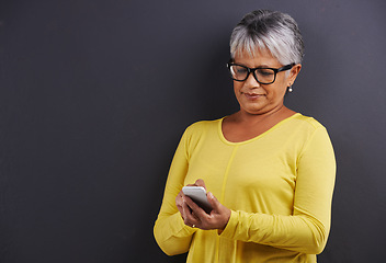 Image showing Glasses, phone and senior woman in studio reading text message, email or blog on internet. Spectacles, technology and elderly female person learning to network on cellphone by black background.