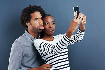 Image showing Love, funny face and couple with selfie in studio for silly, joke or bonding on grey background. Smartphone, app or goofy people hug for blog photography, profile picture or social media comic memory