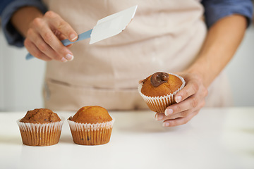 Image showing Hands, person and cupcake with baking, kitchen and spatula for decoration. Baker, muffin and food with countertop, apron and frosting for recipe preparation and recreation or hobby at home or house
