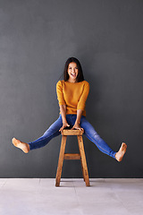 Image showing Portrait, fashion and woman on chair in studio for excited, trendy or casual clothing with gray background. Happiness, cheerful and face of person on stool for wardrobe, sweater and stylish outfit