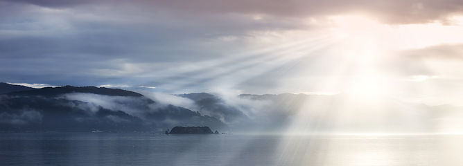 Image showing Sun rays, sea and clouds in blue sky with mountains, water and fog in evening. Lake, landscape and environment for holiday in summer, travel and destination for vacation or peace with scenery