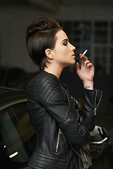 Image showing Female driver, edgy and smoking for thinking, break and insight with car, garage and cigarette. Punk, fashion and model with grunge, vehicle and night for tobacco, choice and decision or mystery