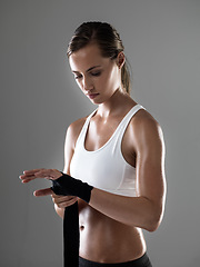 Image showing Woman, fitness and boxer with strapping fists for fight, workout or exercise on a gray studio background. Female person or fighter wrapping hands in preparation or getting ready for sports training