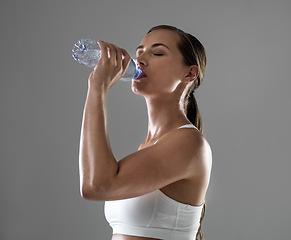 Image showing Woman, fitness and drinking with water for hydration after workout or exercise on a gray studio background. Thirsty female person or athlete with bottle of liquid for natural sustainability on mockup