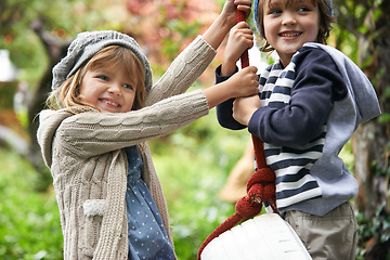 Image showing Children, smile and swing in a backyard in winter together with sibling and fun in garden. Youth, nature and excited on tire in fall at home outdoor with kids playing by tree with happy girl and boy