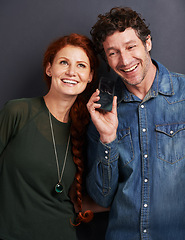 Image showing Happy couple, phone and listening with call or voice note for communication or funny joke on a dark studio background. Man and woman with smile on mobile smartphone for online conversation or chat