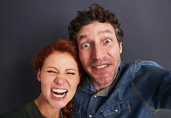 Image showing Selfie, crazy and happy couple in studio together with relationship trust, care and support. Photography, man and woman smile on dark background with commitment, loyalty and affection in fun marriage