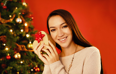 Image showing Portrait, smile and Christmas with woman, gift box and package on a red studio background. Face, person and girl with Xmas parcel and present with surprise and guessing with giveaway prize or holiday