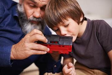 Image showing Grandfather, toy and train with boy child, playing and bonding in family home. Grandpa, young kid and childhood development with games and fun, quality time and love with senior retired man
