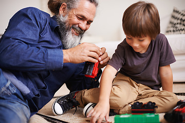 Image showing Grandfather, laugh and toy train with boy child, playing and bonding in family lounge. Grandpa, young kid and childhood development with games and fun, quality time and love with elderly retired man