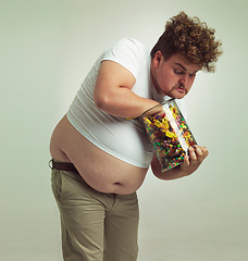 Image showing Candy, sweets jar and man in studio for eating snacks, junk food and dessert in container. Comic, funny and isolated and plus size crazy person with glass for unhealthy diet and sugar on background