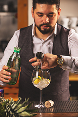 Image showing Bartender pouring gin into glass with ice