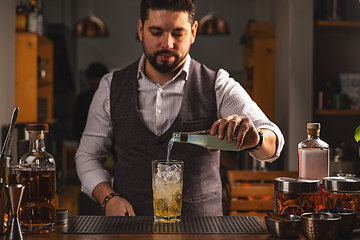 Image showing Professional bartender pours cocktail at bar