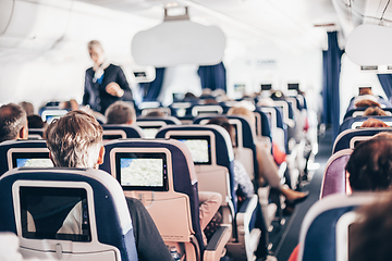 Image showing Interior of airplane with passengers on seats and stewardess in uniform walking the aisle, serving people. Commercial economy flight service concept.