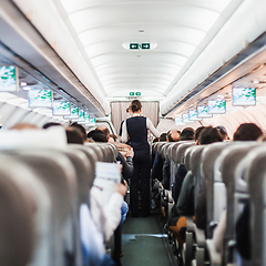 Image showing Interior of airplane with passengers on seats and stewardess in uniform walking the aisle, serving people. Commercial economy flight service concept.