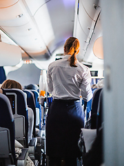 Image showing Interior of airplane with passengers on seats and stewardess in uniform walking the aisle, serving people. Commercial economy flight service concept.