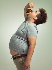 Image showing Fast food, hungry and man with hamburger in studio background with lunch, snack and craving for plus size guy. Male person, burger and takeaway for meal in mouth for eating, starving and bite