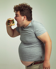 Image showing Obesity, weight gain and fast food for man in studio with burger for unhealthy eating, plus size and greed. Overweight person with meal for mouth and fat stomach for hunger, comedy and bite indoor