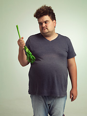 Image showing Plus size, diet and unhappy man with vegetable for health, nutrition and wellness in studio in white background. Weight loss, celery and frustrated male person for healthy food, wellbeing and detox