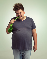 Image showing Obesity, weight gain and humor for man in studio with celery for health eating, nutrition and diet. Overweight person with vegetable in mouth and cry for hungry, and food with vitamin for comic