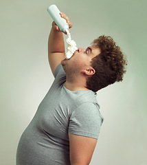 Image showing Plus size, eating and man with cream in studio for unhealthy, sugar and sweet snack or dessert. Messy, greedy and hungry male person enjoying whipped dairy product for humor by gray background.