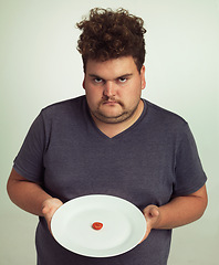 Image showing Portrait, diet or plate and plus size man in studio on gray background, unhappy with size of meal. Food, health or nutrition and disappointed young person frustrated with tiny tomato slice serving