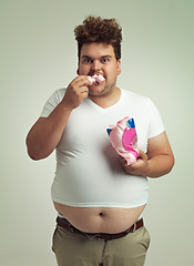 Image showing Portrait, hunger and marshmallow with plus size man in studio on gray background for unhealthy eating. Food, hungry for sweets and candy with young person with snack bag or packet for greed or belly