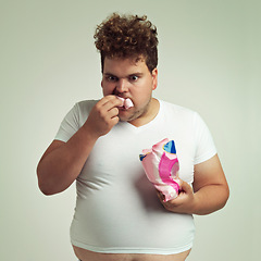 Image showing Food, hungry and marshmallow with plus size man in studio on gray background for unhealthy eating. Hunger, appetite for sweets and ravenous young person with snack bag or packet for greed or gluttony