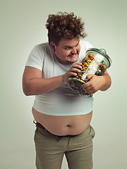 Image showing Candy, crazy and plus size man on a white background for snacks, sweets and dessert in container. Comic, funny and isolated overweight person with glass jar for unhealthy diet or sugar in studio