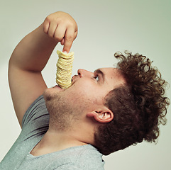 Image showing Overweight, eating and man with chips in studio for unhealthy, potato and salty snack. Plus size, food and profile of male person enjoying stack of crisps in mouth isolated by gray background.