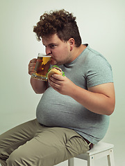 Image showing Man, drink and beer with burger in studio for unhealthy diet, fast food and nutrition on chair. Plus size, hungry and male person with alcohol on stool for dinner, meal and beverage in glass