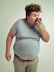 Image showing Obesity, eating and man with cake in studio for unhealthy, sugar and sweet snack. Greedy, overweight and plus size person enjoying messy slice of chocolate dessert isolated by gray background
