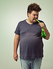 Image showing Plus size, diet and disgusted man eating vegetable for health, nutrition and wellness in studio in white background. Weight loss, celery and unhappy male person for healthy food, wellbeing and detox