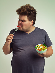 Image showing Man, salad and eating with disgust in studio for healthy diet, nutrition and unhappy for weight loss. Plus size, male person and fork with tomato for vitamin c, detox or organic food for lifestyle