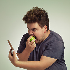 Image showing Guy, apple and chocolate in studio with choice of junk food, sweet or diet for wellness. Plus size, male person eating and decision, fruit or candy for nutrition, lose weight and healthy lifestyle