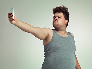 Image showing Selfie, phone and plus size man in studio posing with casual, trendy and cool outfit with stomach. Cellphone, pout and overweight male person with photography picture isolated by gray background.