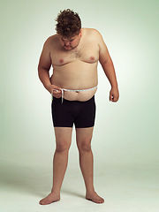 Image showing Man, plus size and tape for measurement in studio on white background for body, progress and weight loss. Looking down, negative and stomach with self care to monitor health and shape to exercise