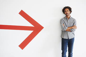 Image showing Man, portrait and arms crossed with arrow by wall in car park with confidence, mockup space and travel. African person, face and serious tourist in parking area with direction, sign and symbol