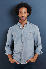 Image showing Black man, portrait and casual for fashion with denim shirt, calm and cool in studio with afro on blue background. African model with smile, pride and pose with hands in pocket and stylish clothes