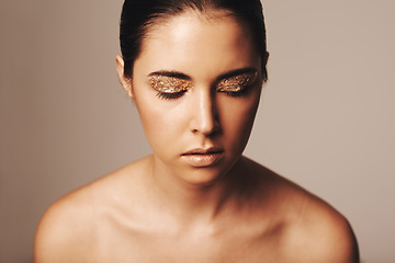 Image showing Woman, makeup and gold glitter on eyes for beauty, cosmetology and glamour with cosmetics on beige background. Eyeshadow, elegance and face model in studio, art or creativity with shimmer and glow