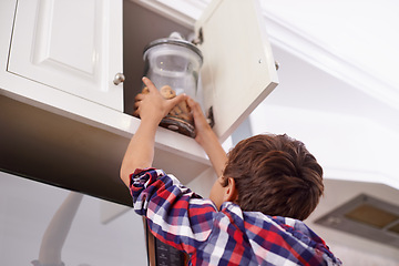 Image showing Kitchen, cupboard and cookie jar with boy child reaching for treats for hunger in home from below. Biscuits, food or snack in glass with young kid in apartment, stealing baked goods to eat from back