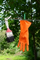 Image showing a paint brush and a rubber orange glove hang on a clothesline 