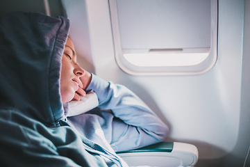 Image showing Tired blonde casual caucasian woman wearing sporty hoodie napping on seat while traveling by airplane. Commercial transportation by planes. Authentic image of real people.