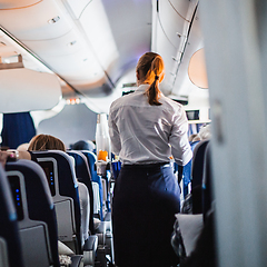 Image showing Interior of airplane with passengers on seats and stewardess in uniform walking the aisle, serving people. Commercial economy flight service concept.