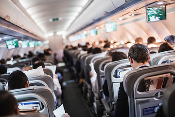 Image showing Interior of airplane with passengers on seats and stewardess in uniform walking the aisle, serving people. Commercial economy flight service concept.