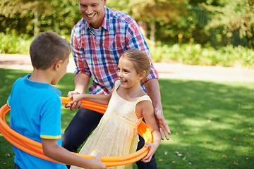 Image showing Father, kids and hula hoop in park for playing, child development and motor skills outdoor. Children, son and daughter with dad in nature for leisure, family time and bonding with smile on grass